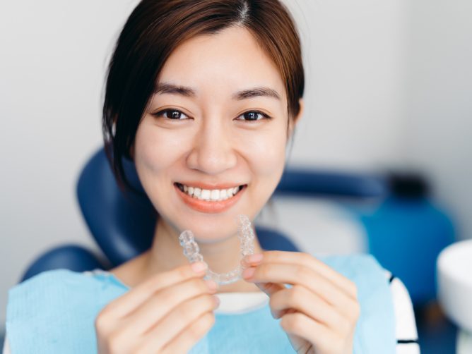 Happy young woman holding Invisalign clear aligners