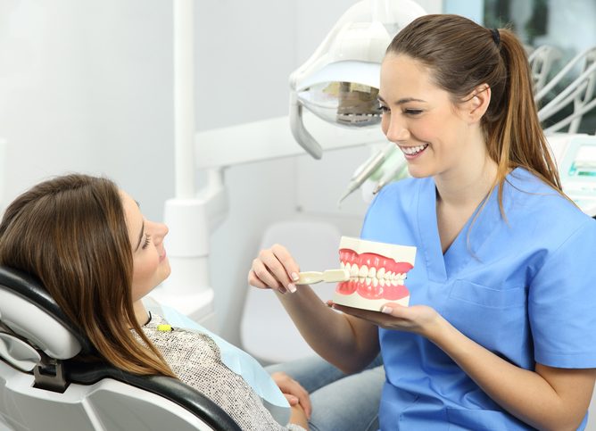 Happy dentist explaining the benefits of teeth cleaning and check-ups to a patient
