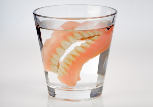 Dentures are seen soaking in a cup. River City Family Dentistry provides Partials and Dentures in Peoria IL.